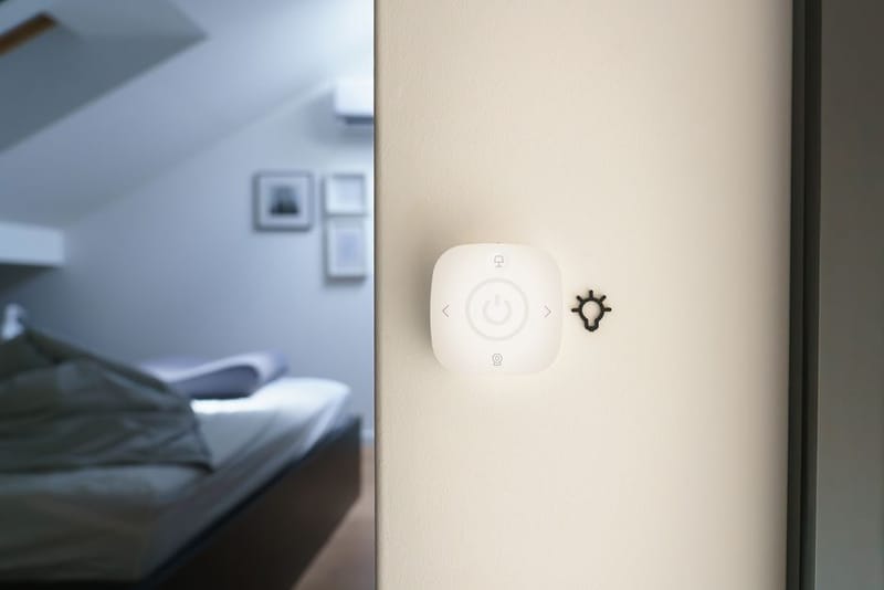 Small smart home control mounted on a wall beside a light switch
